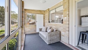 A balcony with a wicker sofa, a window, and a view of the street. - Sunset on Loralyn by Book Jervis Bay (Saint Georges Basin)