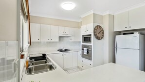 A modern kitchen with white cabinetry, a stainless steel sink, a built-in oven, a microwave, and a refrigerator. - Sunset on Loralyn by Book Jervis Bay (Saint Georges Basin)