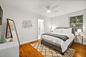 Une chambre à coucher avec un lit, une lampe sur pied, un ventilateur de plafond et une fenêtre avec des stores.