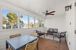A covered patio with a table and chairs, a ceiling fan, and large windows.