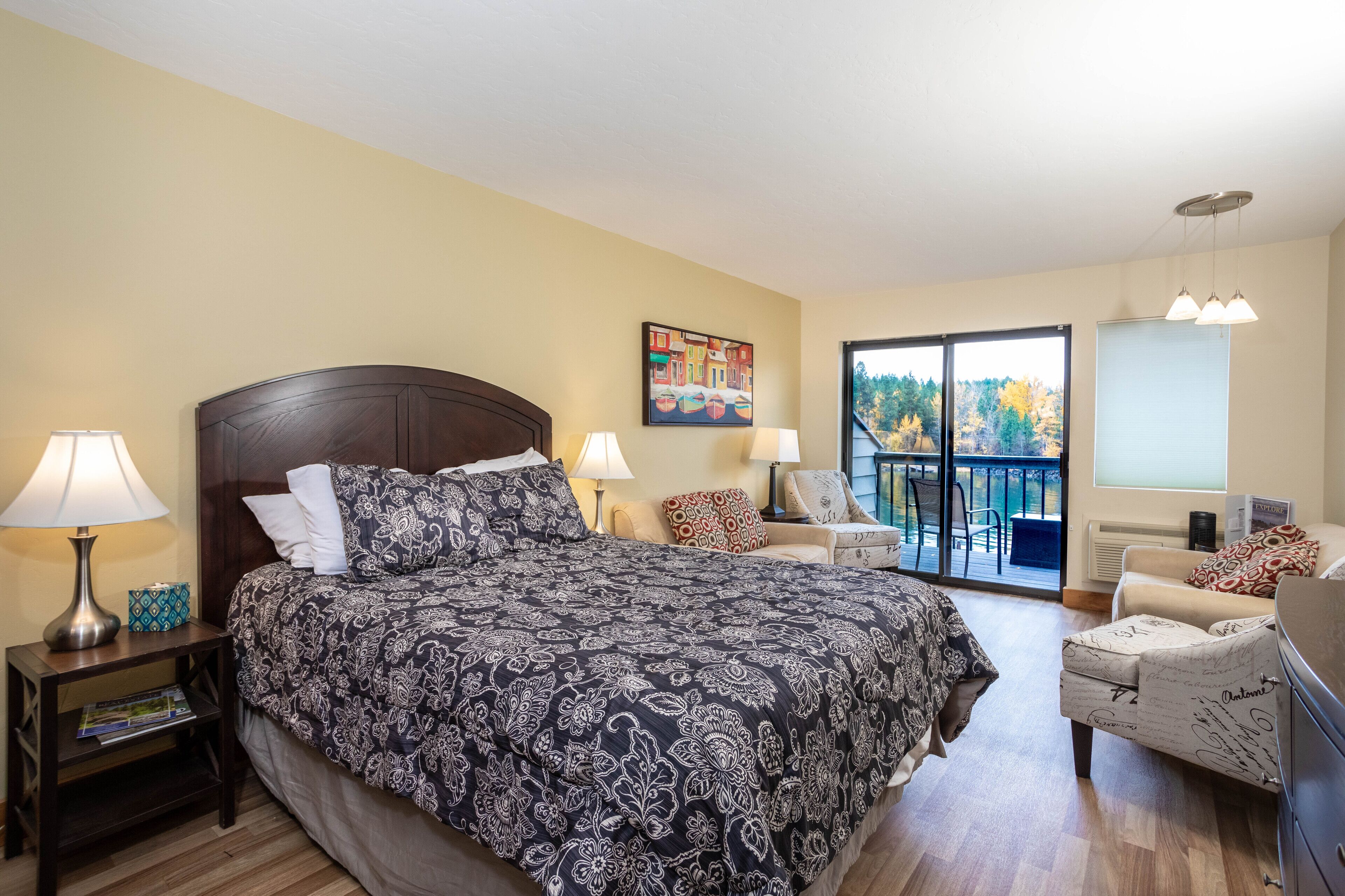A bedroom with a large bed, two bedside tables with lamps, a chair, and a view of the outdoors through a sliding door.