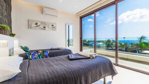 Een moderne hotelkamer met twee bedden, een groot raam met uitzicht op zee en een stenen muur.