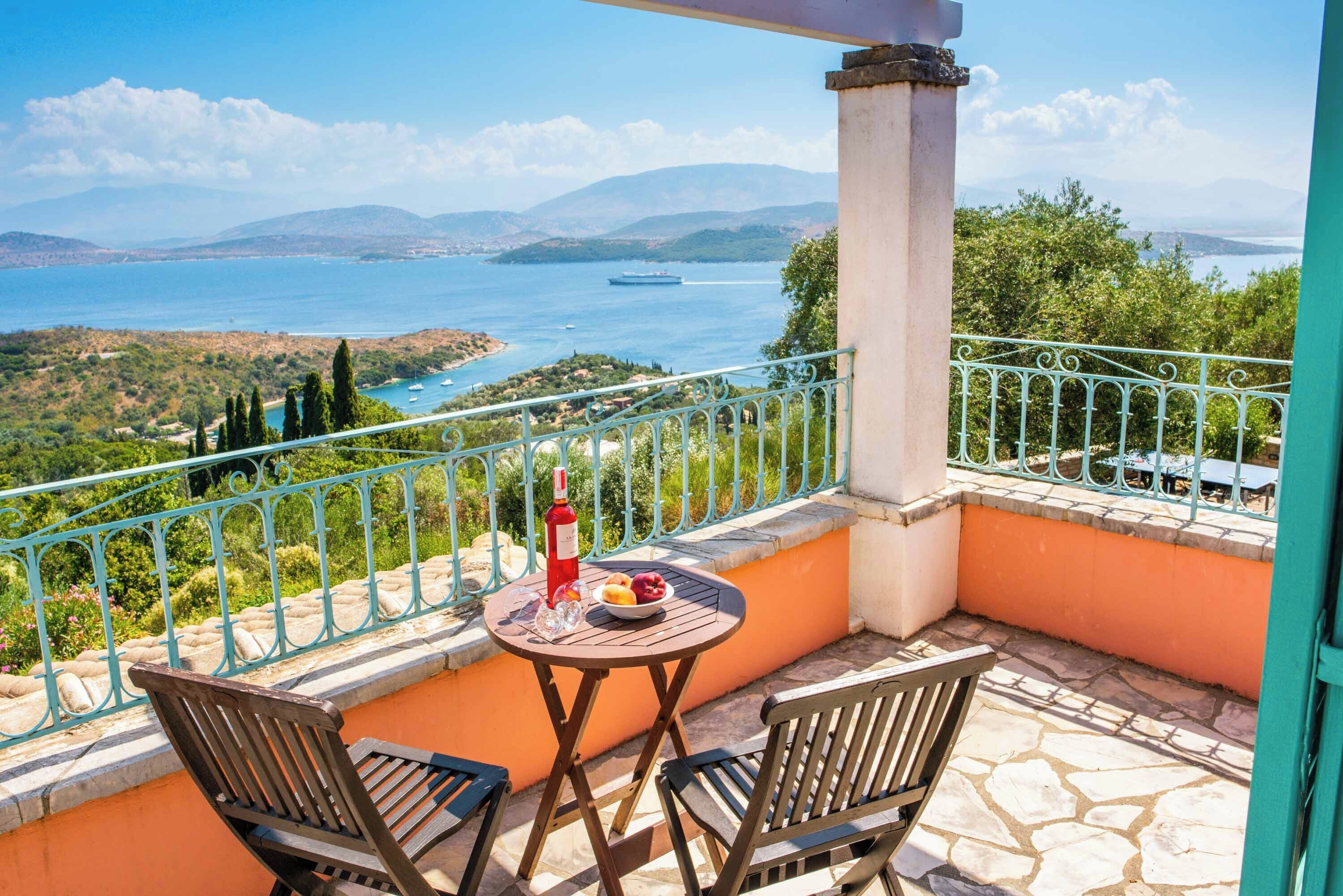 A balcony with a table, two chairs, a bottle of wine, and a bowl of fruit.