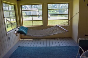 Een hangmat in een kamer met houten vloeren en grote ramen.