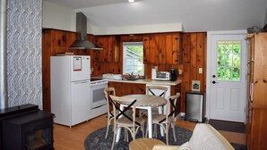 A compact kitchen with wooden cabinets, a white refrigerator, a stove, a microwave, and a small sink. There is a dining table with four chairs. - 3 bedroom home with ac, walk to the beach! (West Dennis)