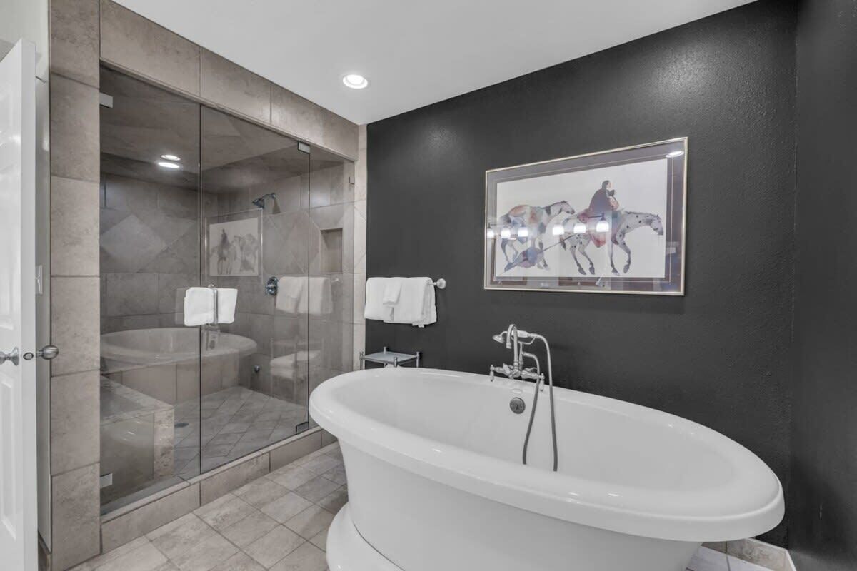 Un baño moderno con una bañera independiente, ducha con mampara de vidrio y una pared oscura con una obra de arte enmarcada.
