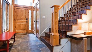 Un escalier en bois avec une balustrade en métal, menant à un palier où se trouvent un banc rouge et une porte.