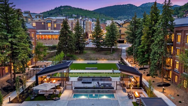 A resort with a swimming pool, outdoor seating, and a view of the surrounding town and mountains. - Modern 2BR Condo - Near Ski Lift; Walk Everywhere! (Park City)