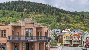 A town with a prominent brick building with a balcony, a sign for Summit and Stethys, and colorful houses in the background. - Modern 2BR Condo - Near Ski Lift; Walk Everywhere! (Park City)