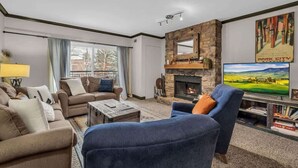 A living room with a fireplace, sofas, a coffee table, and a television. - Modern 2BR Condo - Near Ski Lift; Walk Everywhere! (Park City)
