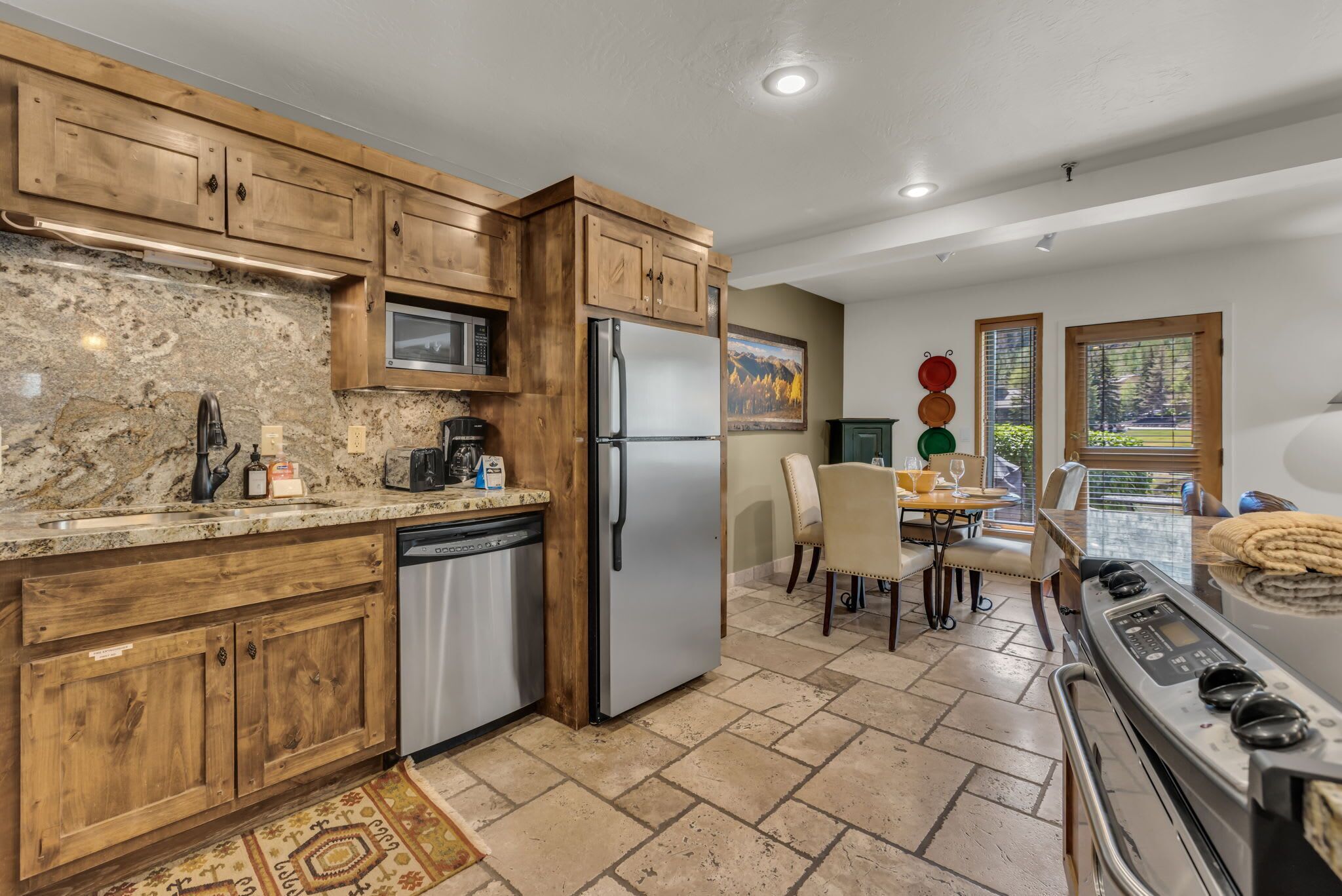 A modern kitchen with wooden cabinets, stainless steel appliances, and a dining area with a view.