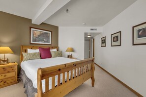 A bedroom with a wooden bed, two bedside tables with lamps, a door, and framed pictures on the wall.