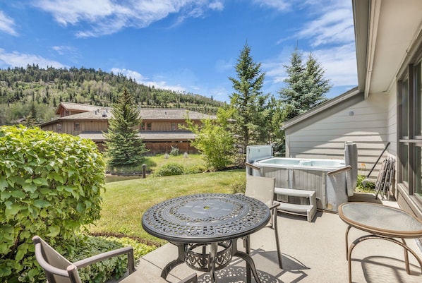 A patio with a round table and chairs, a hot tub, and a view of a mountain and forest.