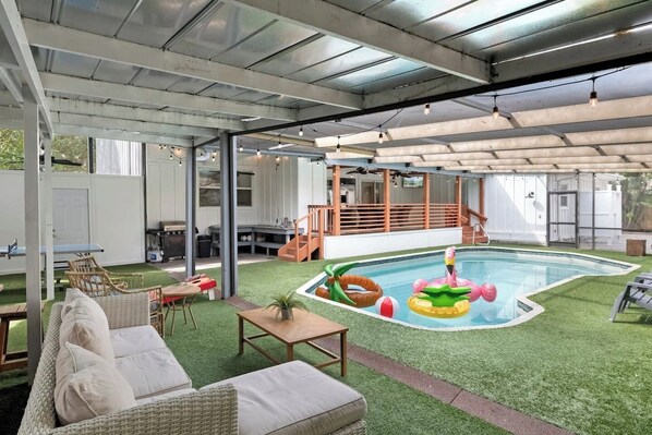 Een overdekt buitengebied met een zwembad, kunstgras en tuinmeubilair.