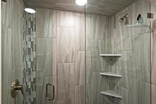 Une douche moderne avec un mur en mosaïque de verre, une étagère intégrée et une douchette à main.