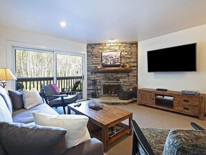 Cozy seating area with a stone fireplace, flat-screen TV, and comfortable sofa and armchairs.