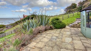 A stone pathway leading to a conservatory with a view of the sea and a distant building.