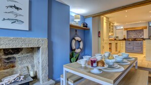 A dining area with a stone fireplace, a blue wall with marine art, and a kitchen with modern appliances.