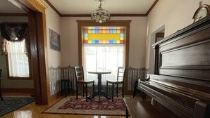 A spacious living room with hardwood floors, a piano, a dining area with chairs, and a stained glass window. - Gateway to the North Shore! Spacious home 2.5 blocks from Lake Superior! (Two Harbors)