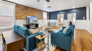 Un salon moderne avec un mur en briques, des canapés bleus, une table basse en bois et un ventilateur de plafond.