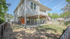 A two-story house with a covered porch, a fenced yard, and a staircase leading to the upper floor. - Pawsitively Paradise: Dog-friendly Home with Fenced Yard Close to Beach, Shops a (Oak Island)