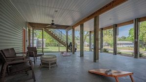 A covered outdoor area with a concrete floor, wooden pillars, wicker furniture, and a staircase leading to an upper level. - Pawsitively Paradise: Dog-friendly Home with Fenced Yard Close to Beach, Shops a (Oak Island)