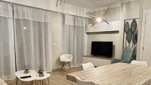En moderne stue med et træspisebord, hvide stole, et fladskærms-tv og en loftventilator.