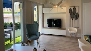 En moderne stue med et stort fjernsyn, en grøn lænestol og en hvid stol.