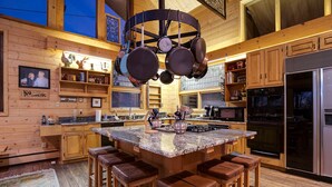 A wooden cabin-style kitchen with a large island, bar stools, and a hanging pot rack. - CP2450 | Breathtaking Views | Ski In/Out | Winter Shuttle (Steamboat Springs)