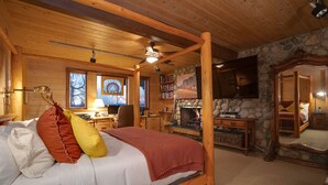 A cozy log cabin bedroom with a four-poster bed, a stone fireplace, a television, and a bookshelf. - CP2450 | Breathtaking Views | Ski In/Out | Winter Shuttle (Steamboat Springs)