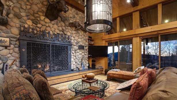 A cozy living room with a stone fireplace, comfortable seating, and a large window offering a view of the outdoors. - CP2450 | Breathtaking Views | Ski In/Out | Winter Shuttle (Steamboat Springs)