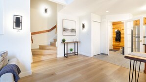 Un intérieur moderne avec un escalier en bois, une console agrémentée de plantes et une vue sur une pièce où se trouve un porte-manteau.
