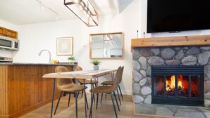 Une cuisine moderne avec une cheminée en pierre, des meubles en bois et un coin repas comprenant une table et des chaises.