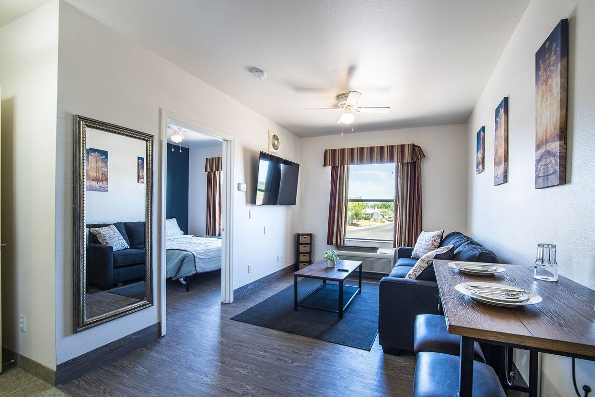 Een moderne woonkamer met een bank, een eettafel gedekt voor twee personen, een flatscreen televisie en een plafondventilator.