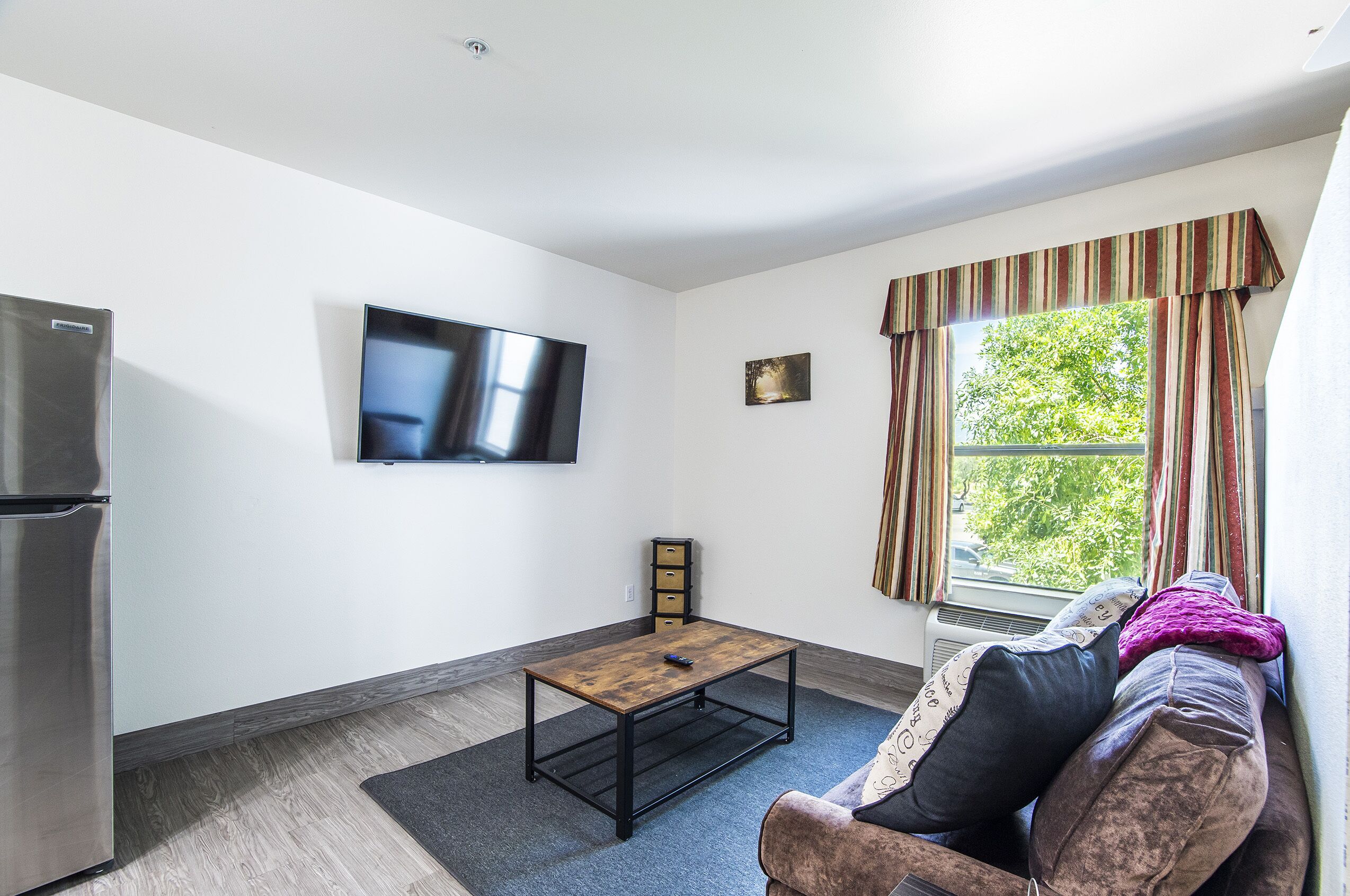 A modern living room with a flat-screen TV, a wooden coffee table, a sofa with cushions, and a window with curtains.