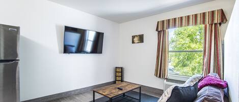A modern living room with a flat-screen TV, a wooden coffee table, a sofa with cushions, and a window with curtains.