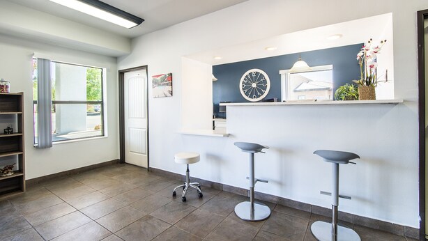 A modern reception area with a large clock, a reception desk, and three bar stools.
