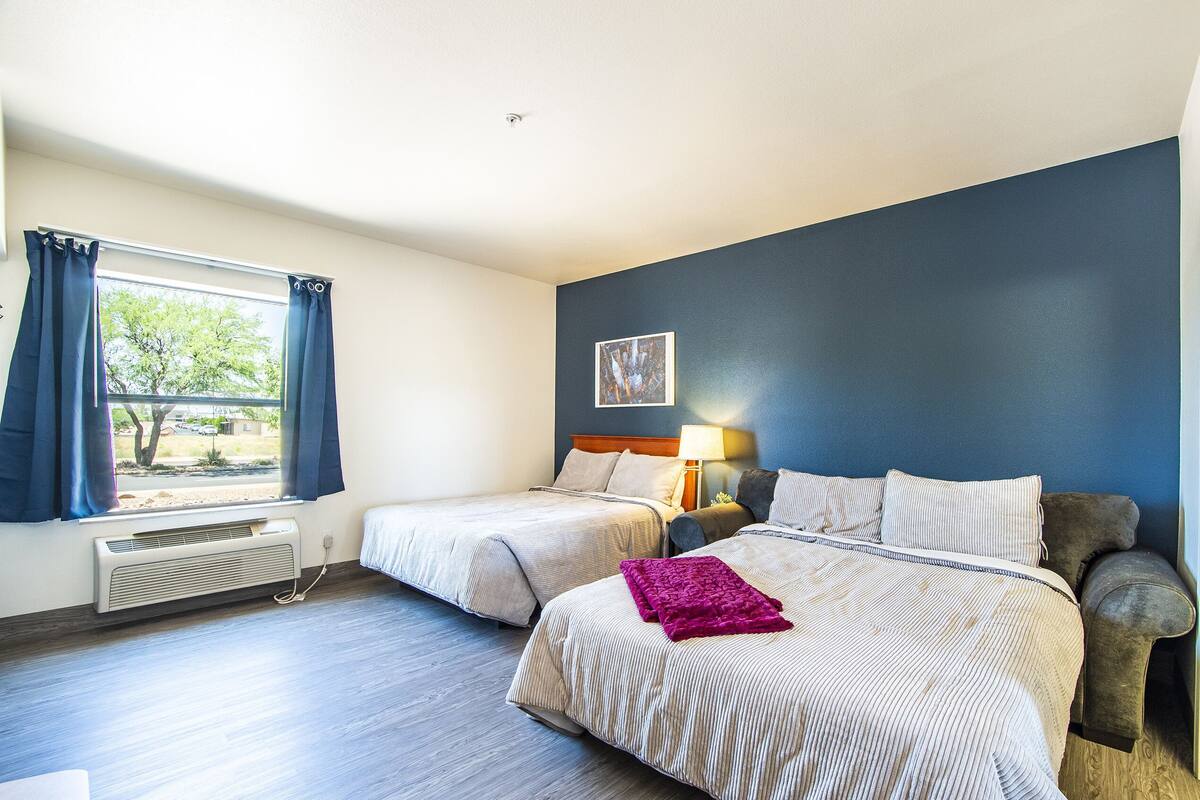 Een hotelkamer met twee bedden, een raam met gordijnen, een verwarming, een lamp en een schilderij aan de muur.