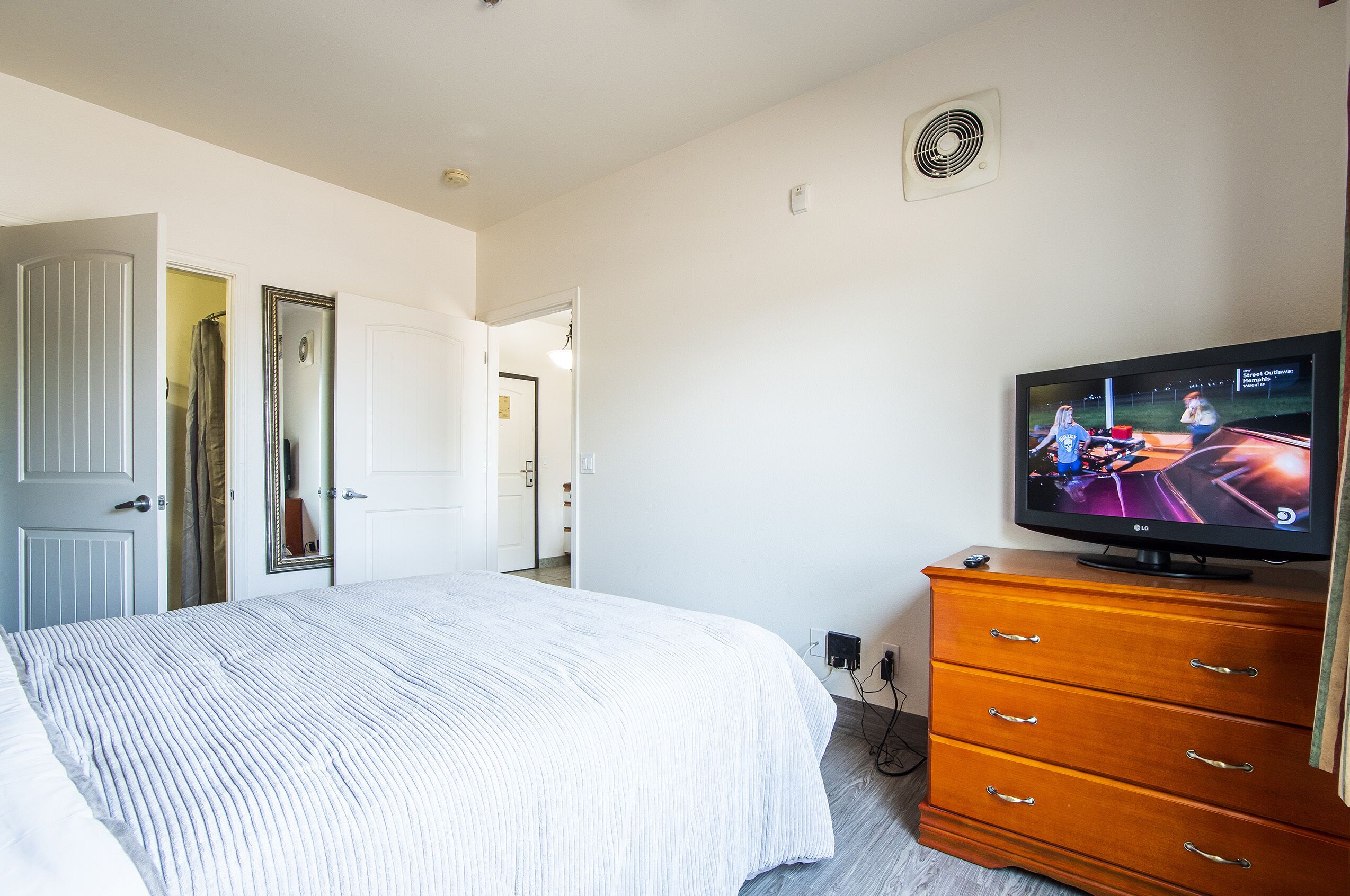 A bedroom with a bed, a dresser, a television, and a door leading to another room.