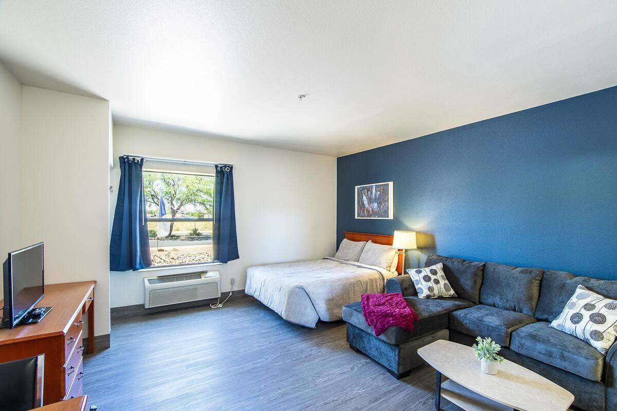 Een moderne hotelkamer met een bed, een bank, een televisie en een raam met gordijnen.