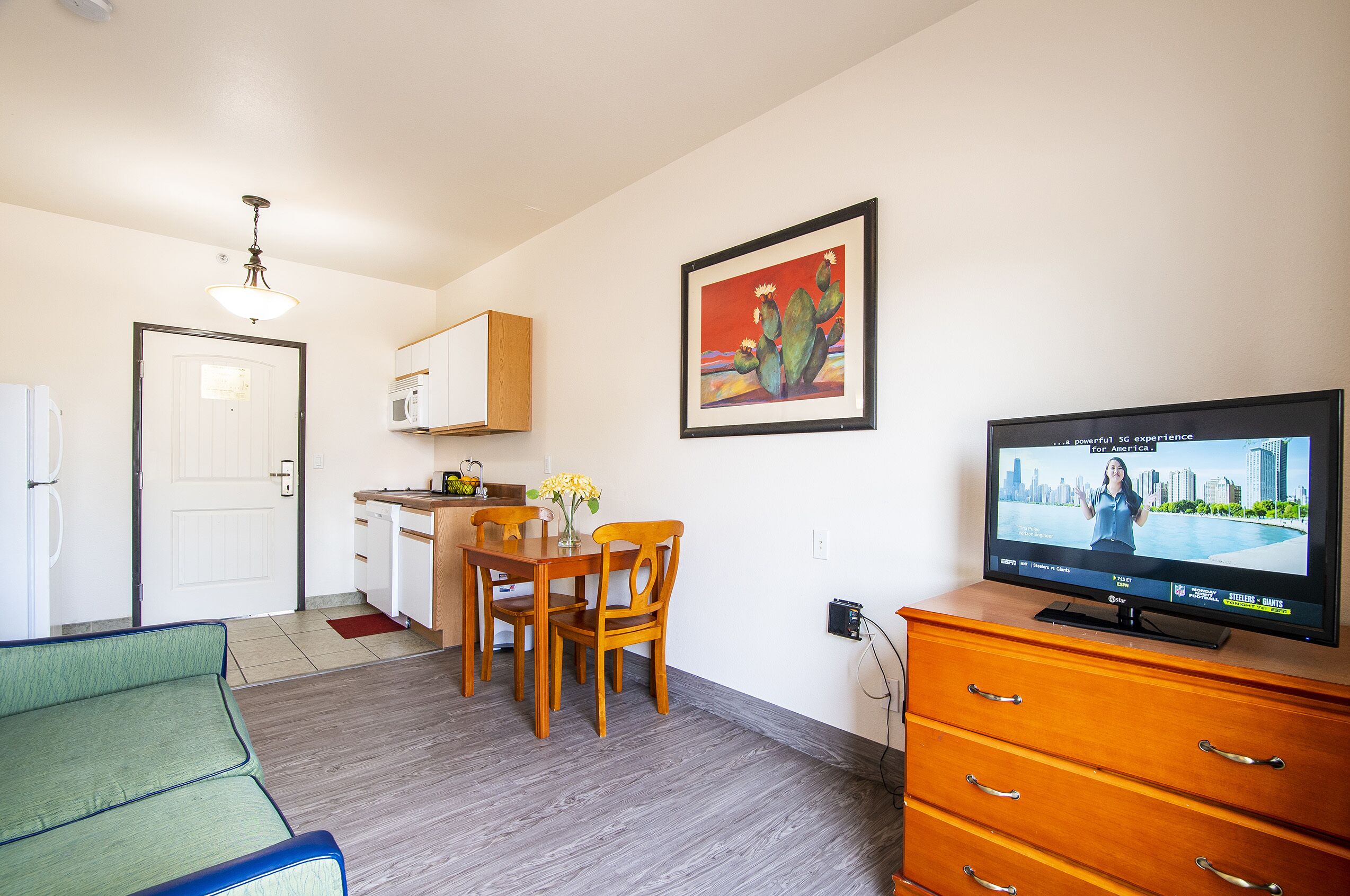 A compact living space with a dining area, kitchenette, and a television displaying a cityscape.
