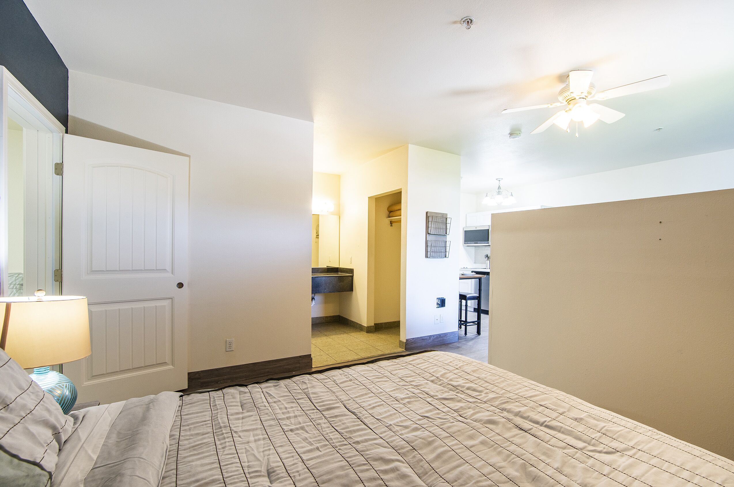A bedroom with a bed, a nightstand, a lamp, and a door leading to a bathroom.