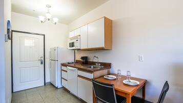 A compact kitchen with white cabinets, a microwave, a sink, and a dining table with chairs.