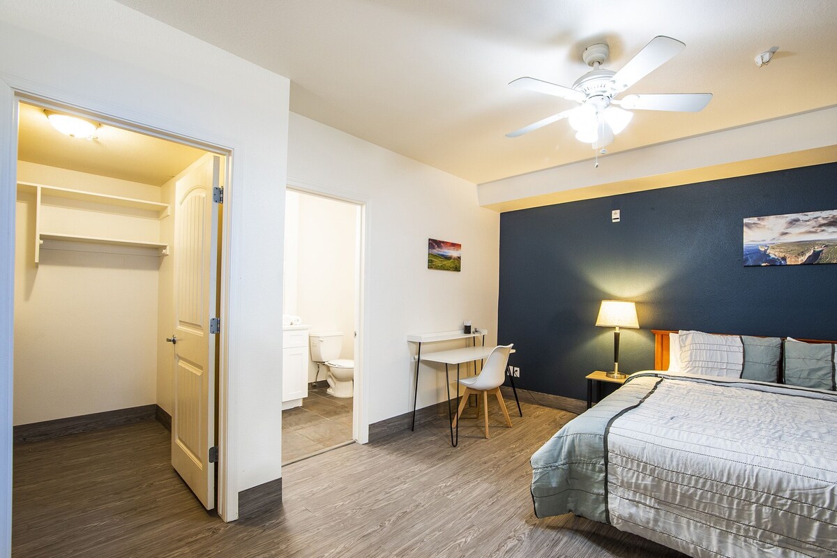 Une chambre d’hôtel équipée d’un lit, d’un bureau, d’une chaise, d’un ventilateur de plafond et offrant une vue sur la salle de bain.