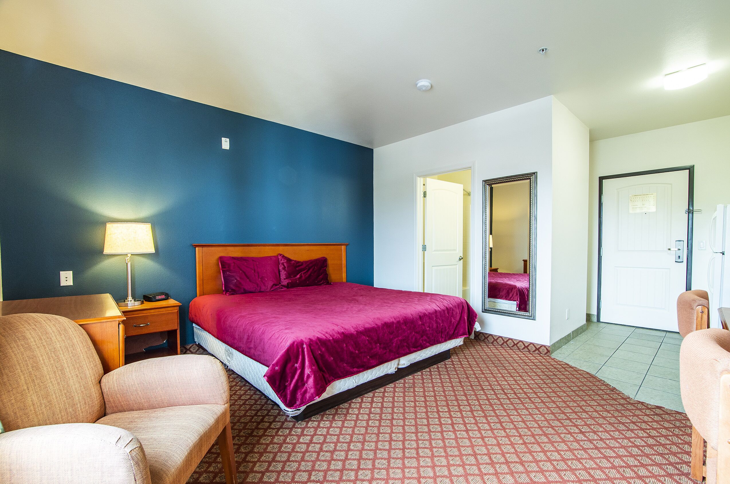 Una habitación de hotel con cama, una silla, una mesita de noche, una lámpara y una puerta.