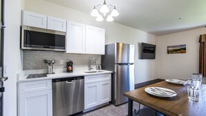 A modern kitchen with white cabinets, stainless steel appliances, a dishwasher, and a dining table set with plates and a glass of water.