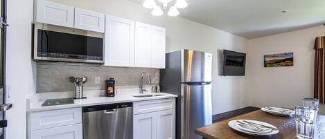 A modern kitchen with white cabinets, stainless steel appliances, a dishwasher, and a dining table set with plates and a glass of water.