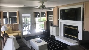 Un salon doté d’une cheminée, d’un ventilateur de plafond et d’un téléviseur fixé au-dessus de la cheminée.