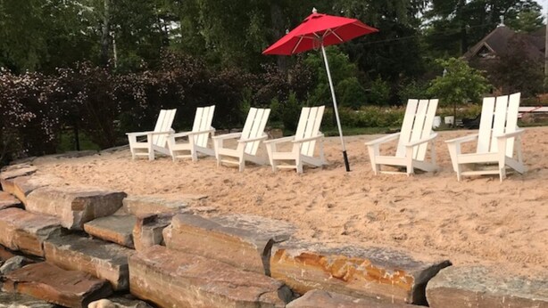 Une plage avec des chaises longues blanches et un parasol rouge.