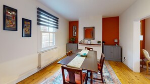A dining area with a table, chairs, a radiator, a window with blinds, and artwork on the walls. - Mill House | Oxford Holiday Let | 2 Beds & Sleeps 4 (Oxford)